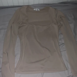 Beige långärmad topp - Säljer en oanvänd helt ny snygg beige långärmad topp i ett mjukt och stretchigt material. Perfekt för en enkel och elegant look. Toppen har en rund halsringning och en figurnära passform.