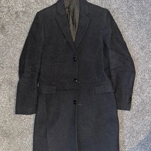 Svart ullblandad rock från MANGO MAN - Snygg svart rock från MANGO MAN i ullblandning. Rocken har en klassisk design med knappar framtill och en stilren krage. Perfekt för kyligare dagar.