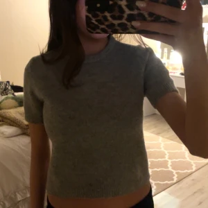 Grå stickad tröja från Zara - Säljer en stilren grå stickad tröja från Zara. Tröjan har korta ärmar och en rund halsringning, perfekt för en avslappnad look. Den är mjuk och bekväm, idealisk för kyligare dagar.