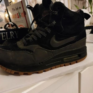 Svarta Nike sneakers - Snygga svarta Nike sneakers med hög design och snörning. Skorna har en robust sula och är perfekta för en sportig look. De har en diskret Nike-logga på sidan och är gjorda i syntetmaterial.