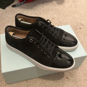 Svarta sneakers från Lanvin - Snygga svarta sneakers från Lanvin med glansig tå och vit sula. Skorna har snörning och kommer i originalförpackning med dustbag. Perfekta för en stilren look. Dom e använd 1 gång och är i 10/10 skick säljer dom för att dom inte passade mig kan bytas ut mot lanvins i storlek 43