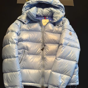Ljusblå pufferjacka från Moncler - Moncler Maya i färgen baby blue, storlek 1. Skick: 7.5/10, en lite flaw visad på bild 3. Endast jackan medföljer