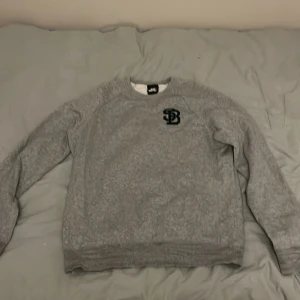 Grå sweatshirt från Nike SB - Säljer en grå sweatshirt från Nike SB med ett svart broderat SB-märke på bröstet. Tröjan har långa ärmar och en rund halsringning. Skön sweatshirt