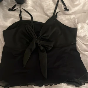 Svart linne med knyt - Snygg svart linne med knyt framtill och justerbara axelband. Perfekt för en stilren look.