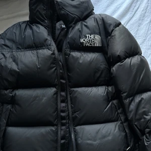 Svart pufferjacka från The North Face - Säljer en svart pufferjacka från The North Face. Jackan har en hög krage och dragkedja framtill. Perfekt för kalla dagar med sin vadderade design.