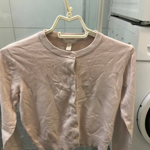 kofta från h&m - Säljer en söt ljusrosa kofta från Hm. Den har långa ärmar och knappar framtill. Perfekt för lager-på-lager-stil eller som ett lättare lager under kyliga dagar.