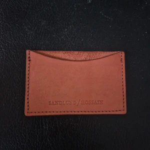 Brun plånbok från Sandlund/Hossain - Snygg och stilren brun plånbok i skinn från Sandlund/Hossain. Perfekt för att hålla dina kort organiserade. Enkel design med en ficka på framsidan.