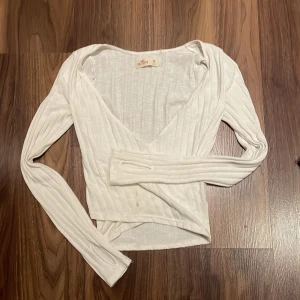 Vit ribbad topp från Hollister - Säljer en vit ribbad tröja/topp i storlek XS. Tröjan har 2 små smink fläckar nertill vilket man kan se på bilderna. Fläckarna går tyvärr inte bort i tvätten så därför säljer jag denna tröja billigt 
