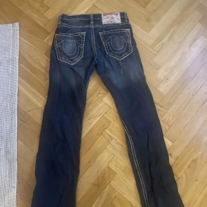 Mörkblå jeans från True Religion - Säljer ett par mörkblå jeans från True Religion med kontrastsömmar och klassisk femficksdesign. Jeansen har en normal passform och är tillverkade i USA. Perfekta för en avslappnad stil. Storlek är 29 midja. 32 längd 