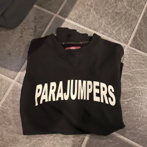 Svart sweatshirt från Parajumpers - Säljer en svart sweatshirt från Parajumpers med vit text på bröstet och ett sytt märke på armen. Tröjan har långa ärmar och en bekväm passform, perfekt för lite kallare dagar. Köpt för cirka ett år sedan för 2400kr, välbevarad.