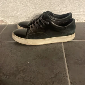 Svarta sneakers från Lanvin - Snygga svarta sneakers från Lanvin med snörning och vit sula. Perfekta för en stilren look. Skorna kommer med en praktisk tygpåse för förvaring.