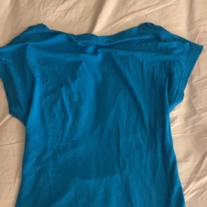 Blå topp - Säljer en enkel blå topp med korta ärmar. Perfekt för en avslappnad stil. Öppen rygg