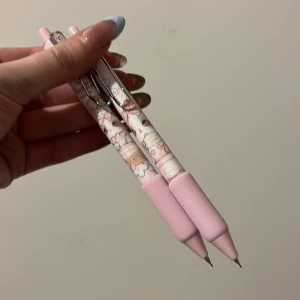 Rosa mekaniska pennor med mönster - Två söta mekaniska pennor i ljusrosa med ett gulligt mönster av tecknade figurer. Pennorna har ett bekvämt grepp och en metallklämma för enkel fastsättning. Perfekta för skolarbete eller dagligt bruk. Priset är för båda 2