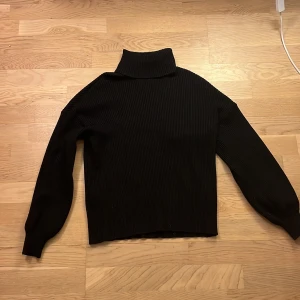 Svart stickad polotröja från Bik Bok - Säljer en stilren svart stickad polotröja från Bik Bok. Tröjan har en hög krage och långa ärmar, perfekt för kyligare dagar. Den ribbade strukturen ger en snygg och modern look.