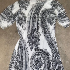 Vit och svart mönstrad blus - Snygg vit blus med svart paisleymönster. Den har korta ärmar och en figurnära passform som framhäver silhuetten. Perfekt för en stilfull look.