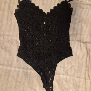 Svart spetsbody från H&M - Snygg svart spetsbody från H&M med smala axelband och v-ringad design. Perfekt för en elegant look med fina spetsdetaljer som ger en lyxig känsla.