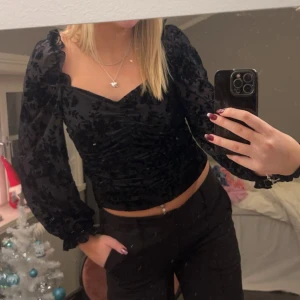 Svart sammetstopp med puffärmar - Snygg svart topp med puffiga långärmar och fyrkantig urringning. Toppen har ett vackert blommigt mönster av sammet och en åtsittande passform som framhäver figuren. Perfekt för en festlig kväll!💫✨ Nypris 400kr
