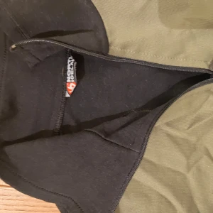 Grön och svart tröja från 66 North - Snygg grön och svart tröja från 66 North med halv dragkedja. Perfekt för utomhusaktiviteter med sin funktionella design och bekväma passform.