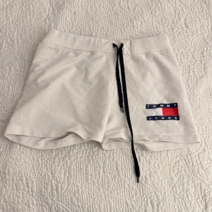 Vita shorts från Tommy Hilfiger Jeans - Säljer ett par vita shorts från Tommy Jeans med en snygg logga på sidan. De har en bekväm resårmidja och svarta snören. Står XXL men sitter snarare som S/M. 