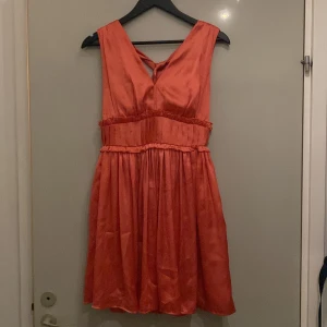  Finklänning från Dry Lake - Silkesklänning. Persikofärgad/rosa, färgen stämmer bäst på sista bilden. V-ringad fram och ännu djupare v-ringning bak. Band att knyta i nacken. Slutar en liten bit ovanför knäna.