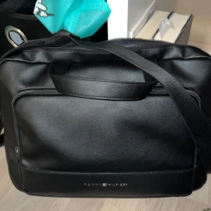 Svart datorväska från Tommy Hilfiger - Säljer en stilren och praktisk marin blå datorväska från Tommy Hilfiger. Den har både handtag och en axelrem. Perfekt för både jobb och skola!  Små defekter förekommer, syns på bild😊Nypris 1400:-