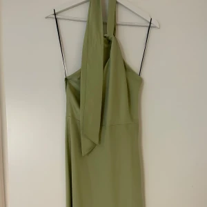 Grön satinklänning halterneck  - Grön klänning i satin med öppen rygg och knytning runt halsen. Aldrig använd 