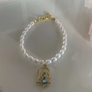 Pärlarmband med hängsmycke - Superfint armband med vita pärlor och ett gulligt hängsmycke i guld och blått. Perfekt för att ge en söt och elegant touch till din outfit. Hängsmycket har en charmig design som verkligen sticker ut. Passar perfekt till både vardag och fest!