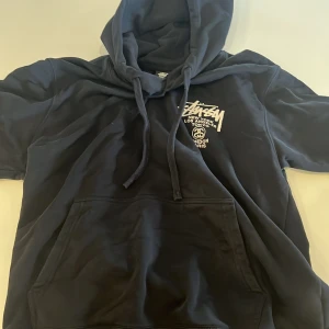 stussy hoodie - Säljer en svart hoodie från Stüssy i storlek S. Den har en stor ficka fram och en cool design med tryck på både fram- och baksidan. Perfekt för en avslappnad stil och passar bra till höst och vinter. Köptes för 1400kr. Vid snabb affär 550kr