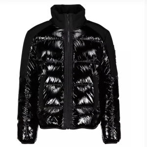 Svart glansig pufferjacka - Säljer en supercool svart glansig pufferjacka från Moose Knuckles. Hög krage och dragkedja. Jackan har en quiltad design och en ficka med en snygg logga på ärmen. Perfekt för att hålla sig varm och stilren under vintern!  