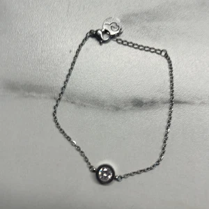 Edblads armband med glittrande detalj - Säljer ett begagnat Edblads armband med en glittrande sten i mitten. Armbandet har en tunn kedja och ett hjärtformat lås som ger en söt touch. Perfekt för både vardag och fest!