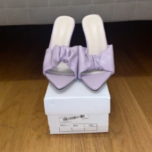 Ljuslila klackskor med spetsig tå - Säljer ett par eleganta ljuslila klackskor med spetsig tå och en snygg rosettdetalj framtill. Skorna har en transparent klack som ger en modern touch. Perfekta för festliga tillfällen!