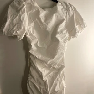 Vit klänning med puffärmar - Säljer en söt vit klänning med puffiga kortärmar och en öppen rygg med knytband. Perfekt för sommarens varma dagar. Man kan se några otroligt vaga fläckar på den, svårt att se i bra ljus (se sista bilden)