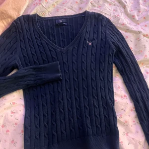 Mörkblå stickad tröja från Gant - Säljer en snygg mörkblå stickad tröja från Gant i stretchig bomull. Tröjan har en v-ringad hals och ett diskret kabelstickat mönster. Perfekt till vardags. 💙