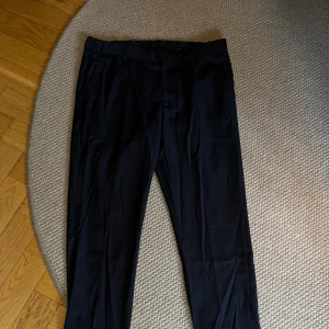 Svarta chinos från H&M - Snygga svarta chinos  från H&M. Perfekta för en stilren look med knapp och dragkedja framtill. Byxorna har en klassisk design med fickor både fram och bak.
