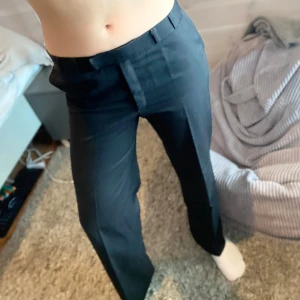 Svarta kostymbyxor - Snygga svarta kostymbyxor med medelhög midja och rak passform. Byxorna har en klassisk design med hällor för bälte och en knappdetalj på ena sidan. pris är förhandlingsbart🥰