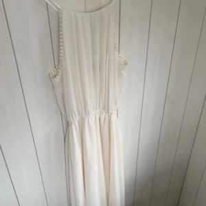 Vit långklänning med knyt -  vit långklänning med knyt i ryggen och fina detaljer längs ärmhålen. Man ser inte på bilden men klänningen är längre