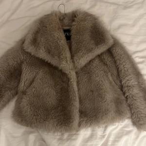 Beige pälsjacka från Zara - Säljer en supermjuk och fluffig beige pälsjacka från Zara. Jackan har en stor krage och är perfekt för att hålla sig varm och stilren under kyliga dagar. Den har en klassisk design som passar till många olika outfits. Ordpris 1500kr.
