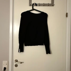 Svart tröja med vita detaljer - Säljer en stilren svart tröja med vita detaljer vid ärmsluten. Tröjan har långa ärmar och en klassisk passform. Materialet är en blandning av viskos, nylon och elastan vilket ger en mjuk och stretchig känsla. Perfekt för både vardag och speciella tillfällen.