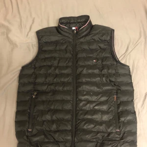 Svart dunväst från Tommy Hilfiger - Snygg svart dunväst från Tommy Hilfiger med dragkedja och quiltad design. Perfekt för lager-på-lager under kyliga dagar. Klassisk stil med diskret logga på bröstet. Den har teckna av skador men fungerar fortfarende dunder🔥