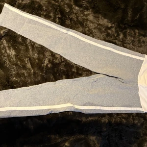 Grå mjukisbyxor med vita ränder - Snygga grå mjukisbyxor från Bia Brazil med vita ränder längs sidorna. Perfekta för en avslappnad stil eller träning. Byxorna har en elastisk midja för extra komfort.