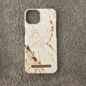 Mobilskal  - Snyggt mobilskal i Carrara Gold design från IDEAL OF SWEDEN, anpassat för iPhone 13. Skalet har ett elegant marmormönster i vitt och guld som ger en lyxig känsla. Perfekt för att skydda din telefon med stil. Aldrig använt för att jag beställde fel storlek, köpte för 400kr💕