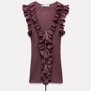 vinröd volangtopp från Zara - Säljer en lila ribbad topp från Zara med volangdetaljer längs ärmhålen och framsidan. Toppen är ärmlös och har en knytning framtill som ger en söt touch. Perfekt för att piffa upp garderoben!