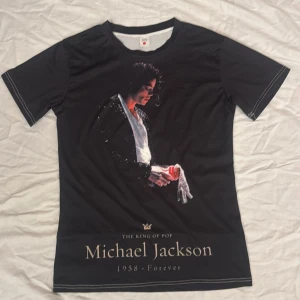 Svart Michael Jackson t-shirt - Snygg svart t-shirt med tryck av Michael Jackson. Texten 'The King of Pop' och '1958 - Forever' finns under bilden. Perfekt för fans av popikonen.