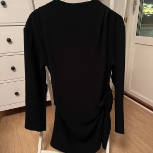 Svart klänning från H&M - Elegant svart klänning från H&M med långärmad design och dragkedja i ryggen. Söm i sidan för att definiera midjan. 