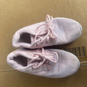 Rosa sneakers med snörning - Säljer ett par ljusrosa sneakers med snörning. Skorna har en enkel och stilren design, perfekt för en avslappnad look. De är tillverkade i ett syntetmaterial som ger en lätt och bekväm känsla.