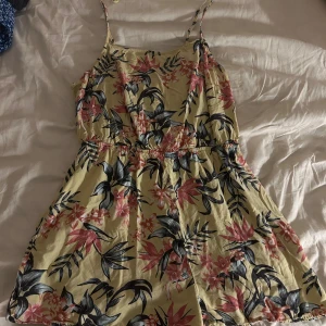 Blommig shorts byx dress med smala axelband - Säljer en söt onepice med blommigt mönster i rosa och grönt på en ljusgul bakgrund. Den har smala axelband och en avslappnad passform, perfekt för varma dagar. 🌸