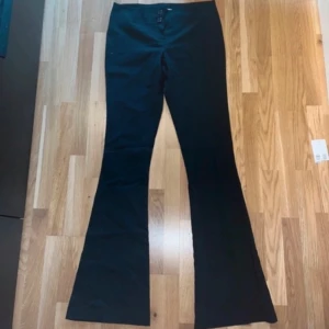 Svarta bootcut byxor - Snygga svarta bootcut byxor med sjukt låg  midja och knappar framtill. Perfekta för en stilren look. Klippta till en person som är ca 160 cm lång 