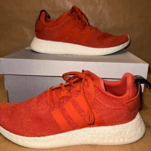  Adidas - Snygga orange sneakers från Adidas med vit sula och klassiska tre ränder på sidan. Skorna har snörning och en bekväm passform, perfekt för vardagsbruk. Storlek 45