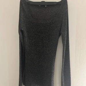 Svart glittrig tröja - Snygg svart glittrig tröja med långärmad design. Perfekt för att lägga till lite glamour till din outfit. Tröjan har en elegant passform och är idealisk för festliga tillfällen.
