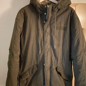 Khakigrön parkajacka från Extreme Blue - Säljer en grön parkajacka från Extreme Blue med huva och dragkedja. Jackan har en mysig fleecefoder och praktiska fickor framtill. Perfekt för kyliga dagar. 🧥